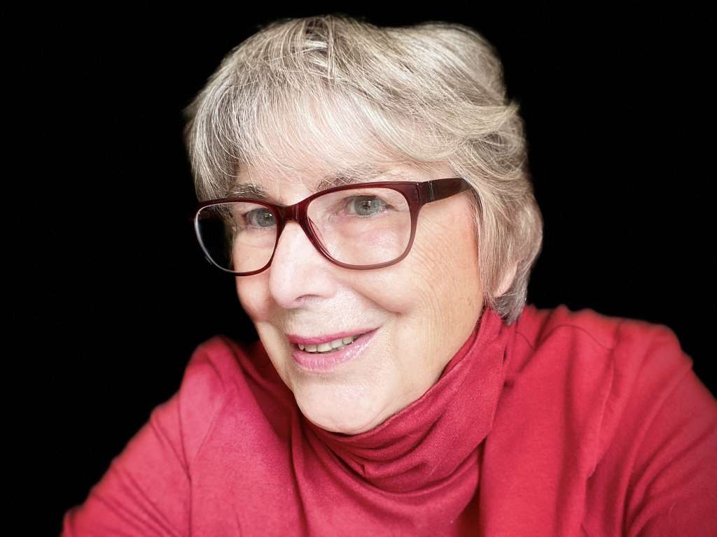 Author Jackie Craven in red turtleneck shirt and dark red glasses.